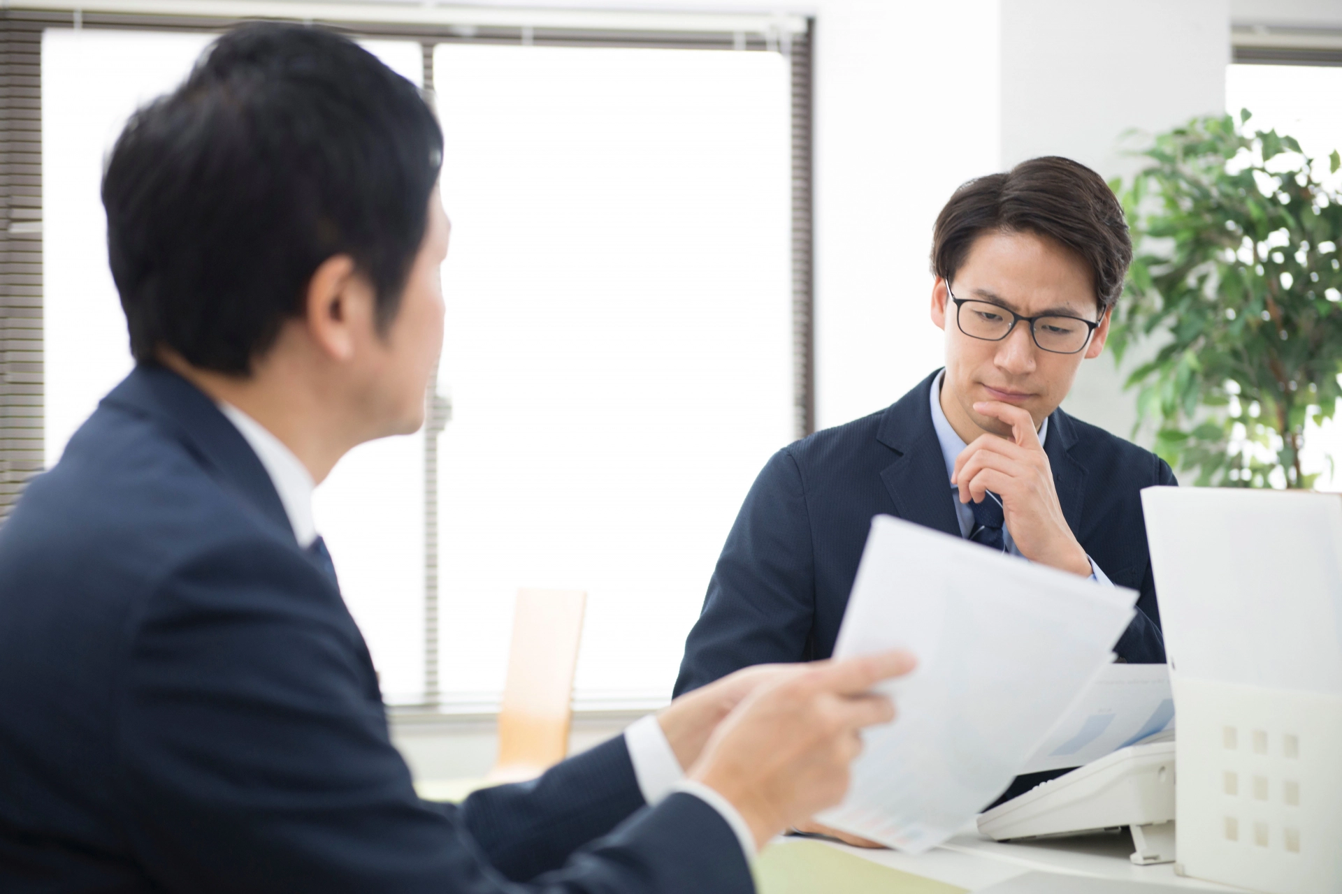 資料を説明するビジネスマンとそれを見て渋い顔の担当者