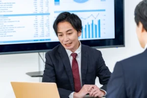 パソコンを見ながら社長に説明する男性